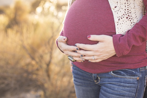 Pregnant woman cradling her growing belly with her hands outdoors in the autumn